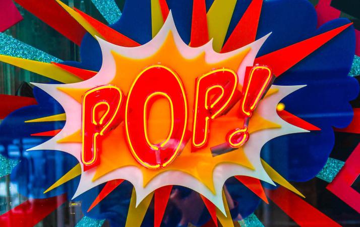 Neonlicht mit dem Schriftzug 'Pop' in Rot-Gelb auf einer bunten Glasscheibe.