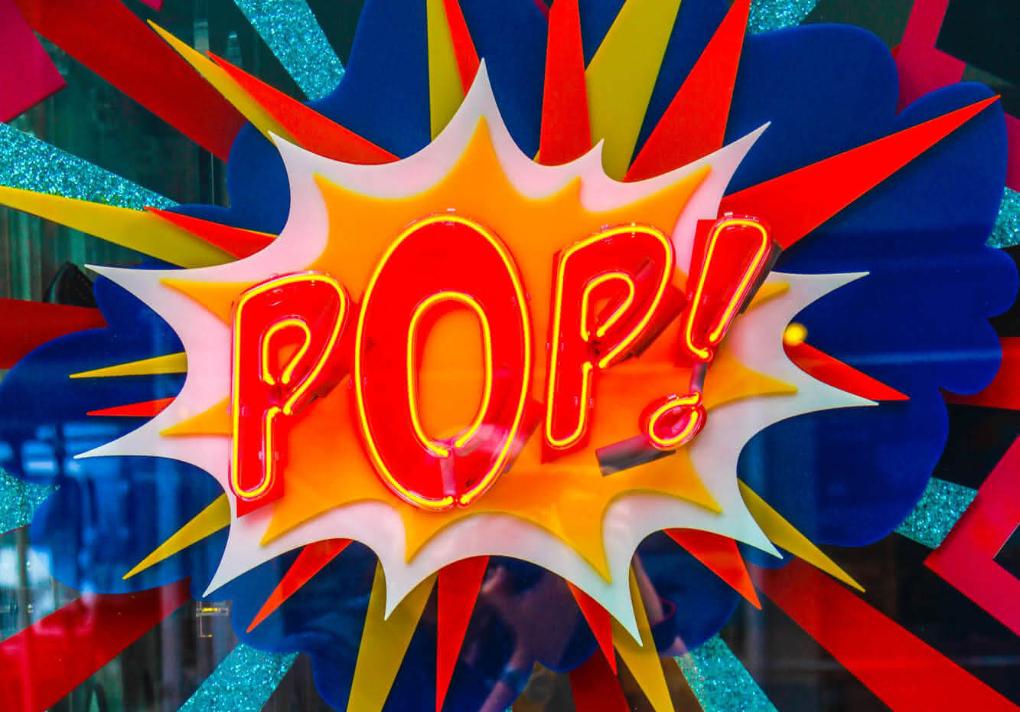 Neonlicht mit dem Schriftzug 'Pop' in Rot-Gelb auf einer bunten Glasscheibe.